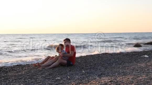 爸爸和两个男孩坐在海滩上儿子们坐在海里视频的预览图