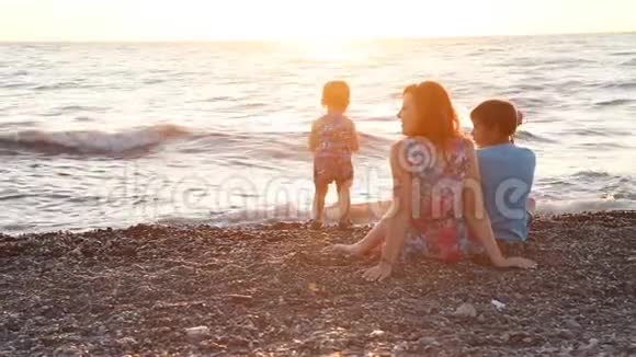 妈妈和两个男孩日落时在海边的海滩上休息视频的预览图
