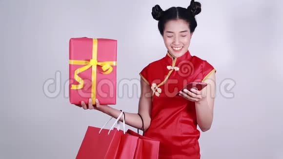 女士穿旗袍带购物袋和礼物使用手机视频的预览图