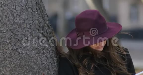 神秘女孩的肖像帽子藏在树附近温暖的天气黑客在公园里用平板电脑4k视频的预览图