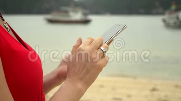 女性的手那个女人手里拿着电话背景是一个有船的海湾美丽的女人视频的预览图