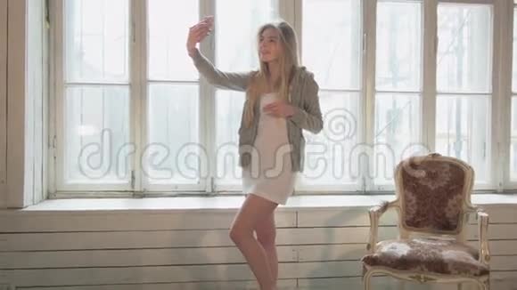 对面窗户上的金发女郎在一间用木头做的白色房间里自拍一个穿着短裙的年轻美女视频的预览图