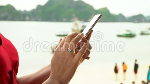 在海滩上游客散步旅游船矗立在海岸女性的手那个女人手里拿着电话对着视频的预览图