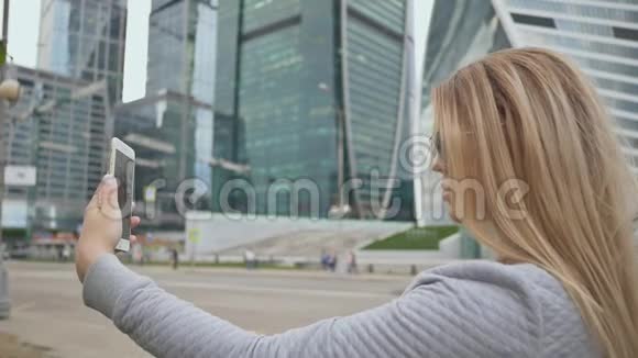 这个女孩正在城市中心的高层建筑背景下自拍视频的预览图