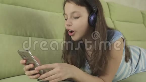 戴着耳机唱着卡拉OK歌的漂亮少女在智能手机股票录像中视频的预览图