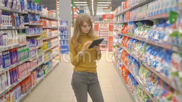 可爱的年轻女士在超市用平板电脑查看购物清单视频的预览图