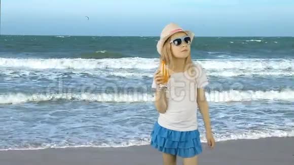 年轻的白种人女孩站着通过吸管喝橙汁鸡尾酒海洋海岸地平线女孩喝橘子视频的预览图