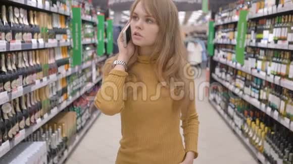 可爱的女人用手机说话决定在超市买什么酒视频的预览图