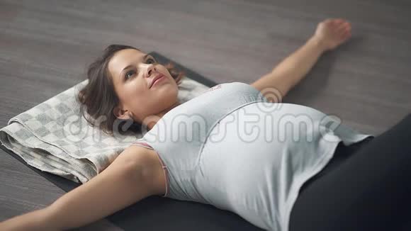 地板上的一位年轻女子正在为怀孕的人做瑜伽视频的预览图