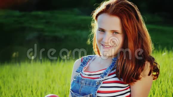 少女的肖像在绿色草地上吃一个大红苹果视频的预览图