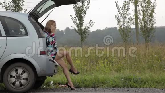 金发女孩坐在她的破车后备箱里在乡间小路上闪烁着紧急信号视频的预览图