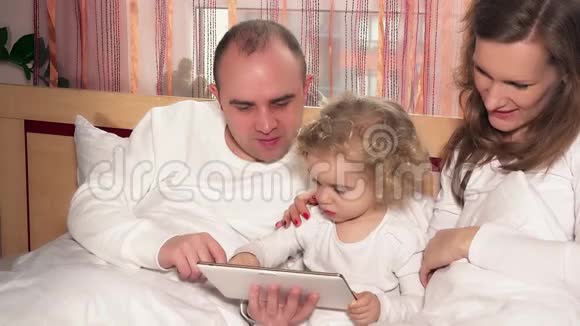 一对夫妇用平板电脑和小女儿上床视频的预览图