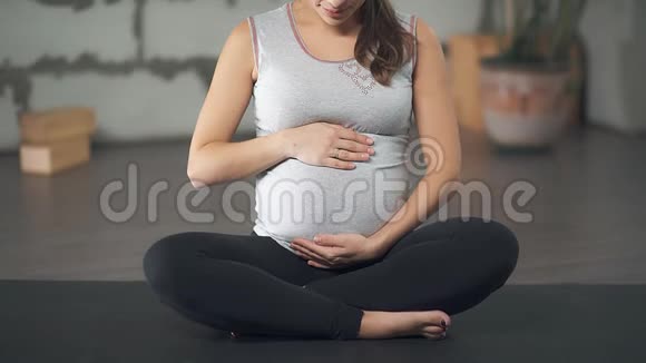 一位孕妇正在抚摸她的腹部坐在瑜伽垫上视频的预览图