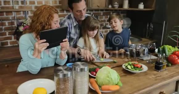 父母教孩子们一起在厨房做饭幸福的家庭用平板电脑一起准备食物视频的预览图