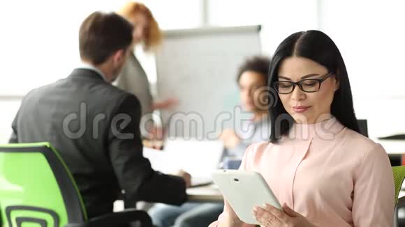 办公室里的团队合作深色头发的女人在前面看着数码平板电脑视频的预览图