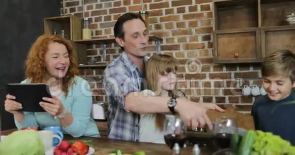 父母教孩子们一起在厨房做饭幸福的家庭用平板电脑一起准备食物视频的预览图