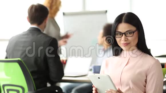办公室的会议室里前景的黑发女人手里拿着平板电脑视频的预览图
