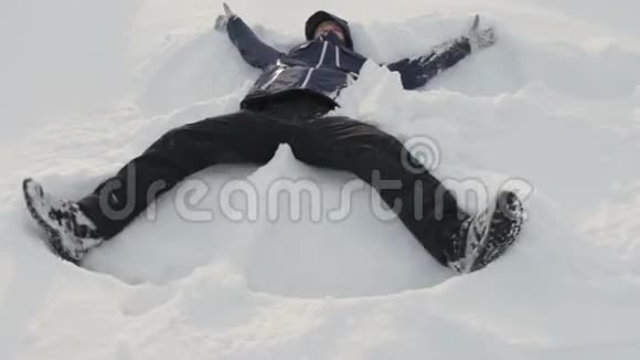 年轻人在阳光下在雪地里玩耍做雪天使玩得开心微笑寒假假日视频的预览图