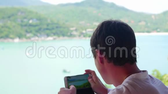 盖伊正在智能手机上从不同的角度拍摄大海和山脉的全景全景视频的预览图