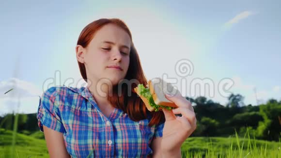 一个脾气暴躁的红发少女在大自然中吃三明治微笑欣赏风景4K慢动作视频视频的预览图