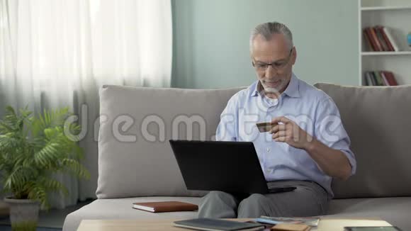 坐在沙发上在笔记本电脑上插入卡号的养老金领取者视频的预览图