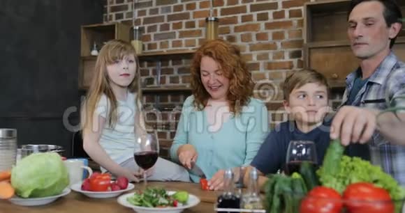 家庭帮助母亲一起做饭父母带着两个孩子在家准备食物在家说话切碎视频的预览图