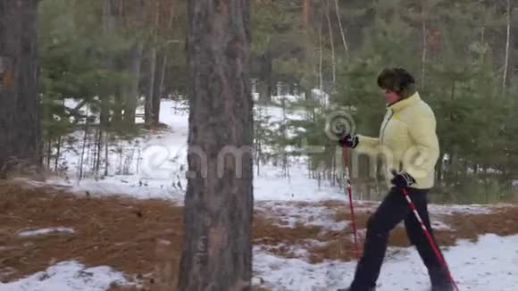 在冬季森林徒步旅行期间训练北欧漫步的高级妇女视频的预览图