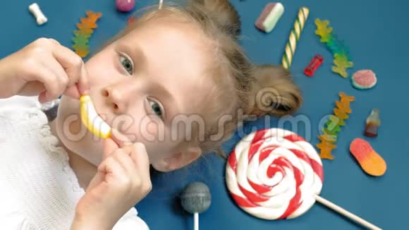 快乐的小女孩躺在蓝色背景上带着糖果特写肖像视频的预览图