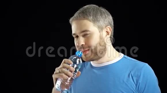英俊的灰发男人穿着蓝色t恤从塑料瓶里喝水黑色背景4K视频视频的预览图