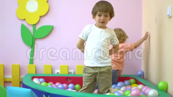 可爱的白人小男孩和小女孩在五颜六色的球池里嬉笑玩耍就学前的视频的预览图