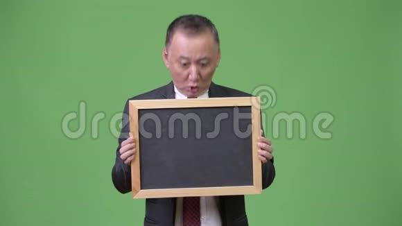 成熟的日本商人绿色背景下拿着黑板视频的预览图