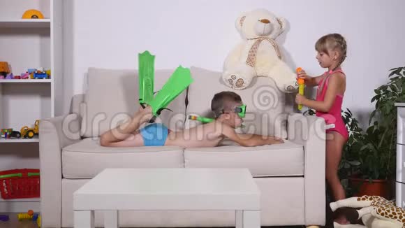 两个穿泳衣的快乐孩子一个戴着潜水面具的男孩在沙发上女孩在房间里吹泡泡视频的预览图