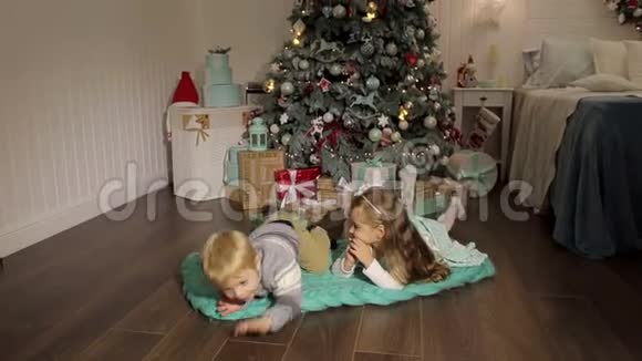 两个孩子躺在圣诞树附近的地板上视频的预览图