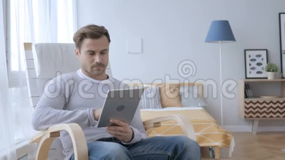 男人坐在休闲椅上浏览平板电脑上的互联网视频的预览图