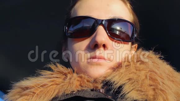 一个戴太阳镜的女孩的特写肖像穿着冬装的年轻女人开着车和别人说话日落视频的预览图