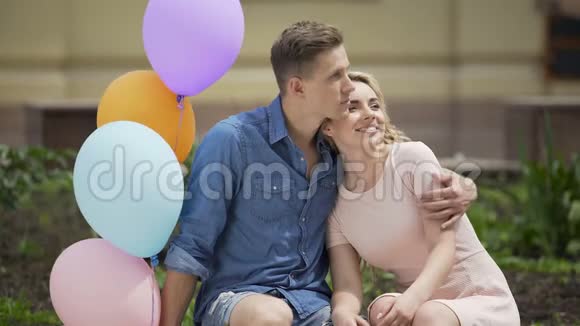 夏天一对情侣在长凳上拥抱一个人拿着气球浪漫的约会视频的预览图