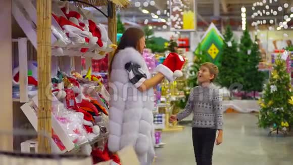 快乐的母亲正把圣诞老人的帽子戴在儿子身上拥抱他在商场里花时间视频的预览图
