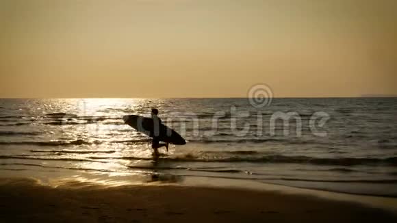 4K在热带海滩日落时年轻快乐的冲浪男子带着长长的冲浪板跑步的剪影海边的冲浪者视频的预览图