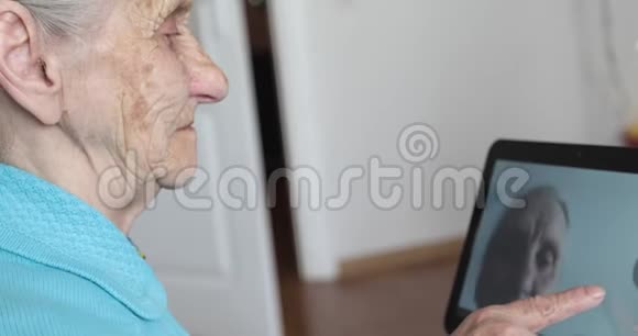 一位头发灰白的老妇人看着电子平板电脑上的照片视频的预览图