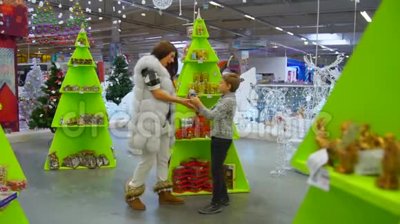 快乐的孩子来到他的母亲身边兴高采烈地展示着雪球圣诞节假期购物中心的位置视频的预览图