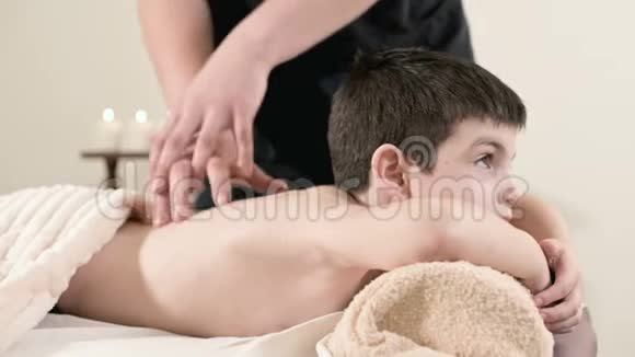 男性理疗师按摩师为躺在按摩床上的小男孩做一个疗愈放松的按摩肩膀和视频的预览图
