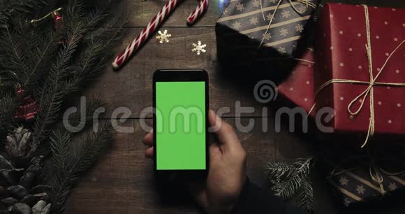 男性手在带有绿色屏幕的黑色智能手机上点击页面铬钥匙上景垂直位置圣诞节视频的预览图