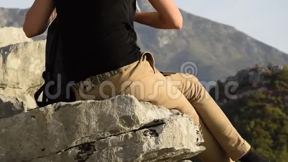 年轻女子在坐在山崖边上的美丽山峰上寻找背包里的东西视频的预览图