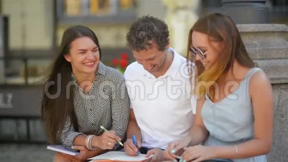 三个学生在户外学习在温暖的晴天在城市里一起笑两个女孩和一个男孩视频的预览图