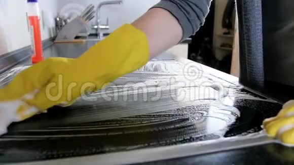 黄色橡胶手套中年轻女性清洁电动感应炉用deteregntsufs的特写慢动作视频视频的预览图