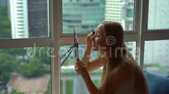 一位年轻女子在市中心的一扇全景窗旁化妆的超慢动作镜头视频的预览图