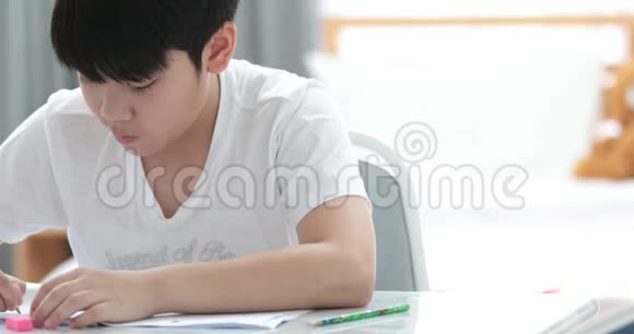 快乐的亚洲可爱男孩手拿铅笔在家写作业视频的预览图