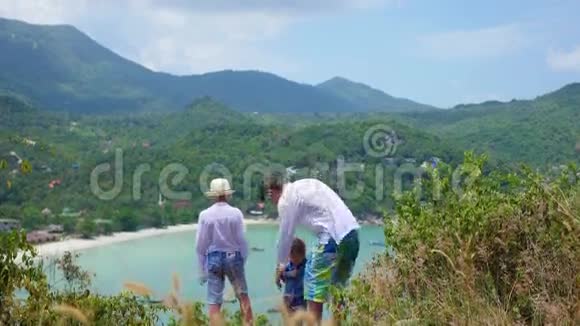 一个年轻人带着两个孩子在海和山的背景下玩耍视频的预览图