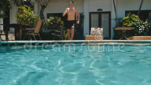 暑假里的年轻人在炎热的晴天跳进蓝色的游泳池里喝点东西一个人在空中潜水视频的预览图