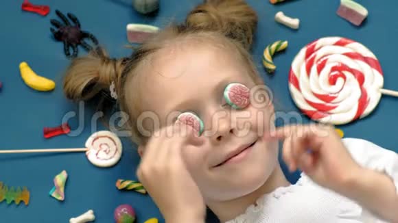 快乐的小女孩躺在蓝色背景上带着糖果特写肖像视频的预览图